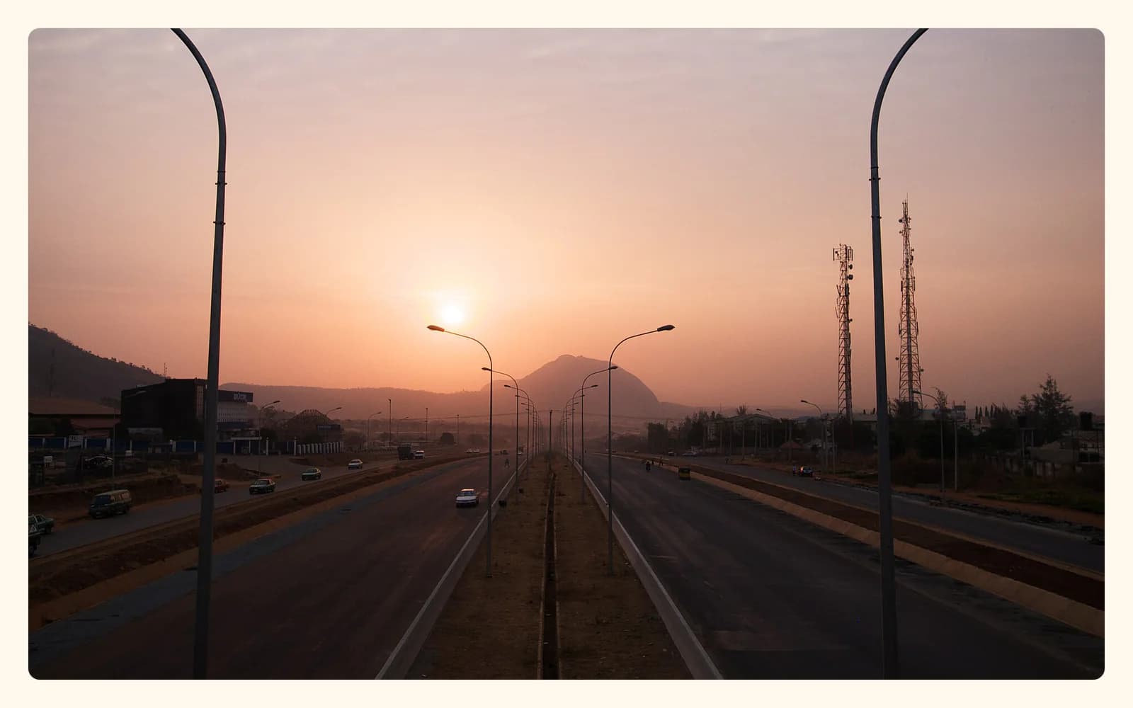 Aso Rock rising behind a broad Abuja roadway at sunrise.