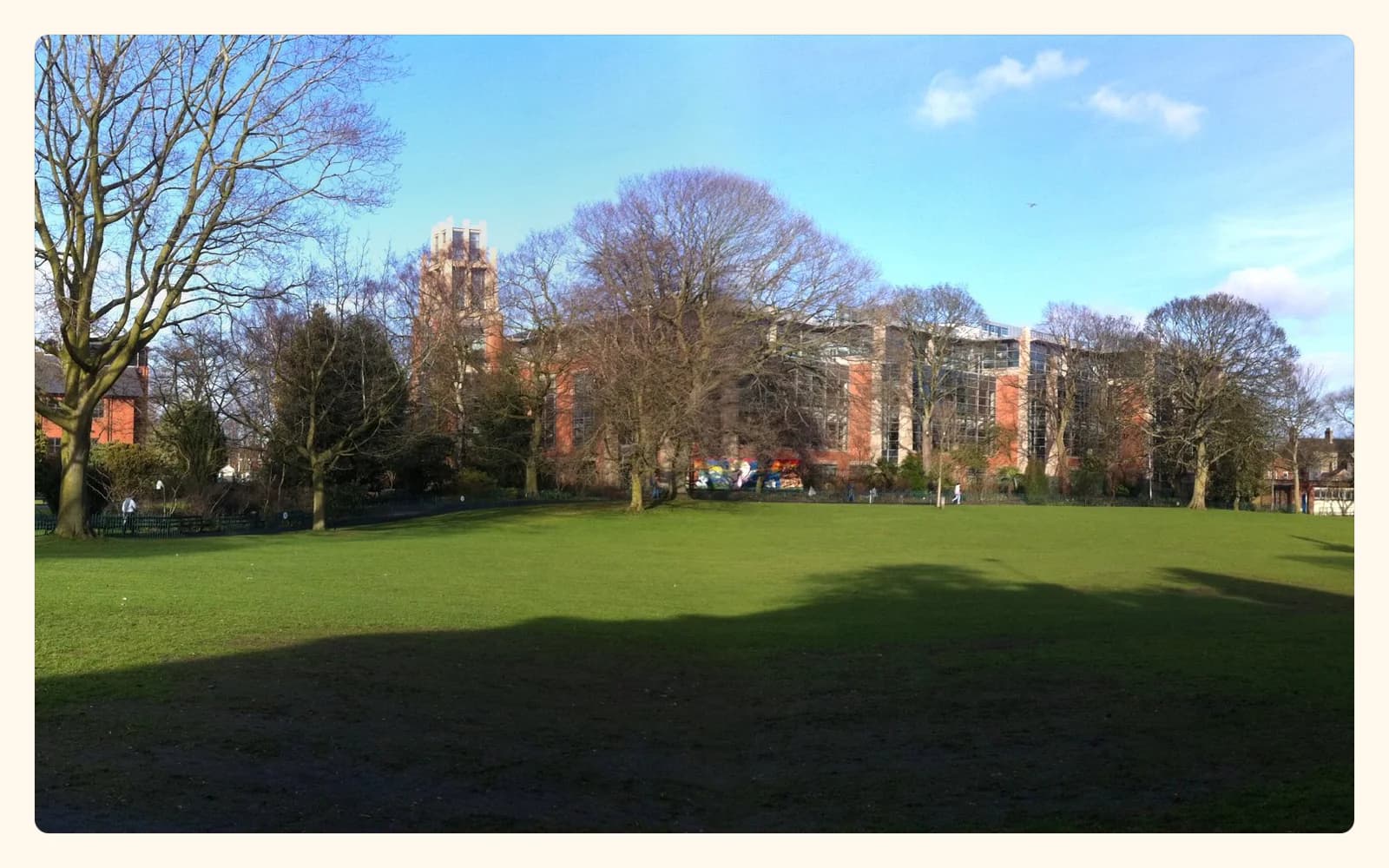 A broad green lawn and mature trees in Belfast’s Botanic Gardens, with university buildings beyond.