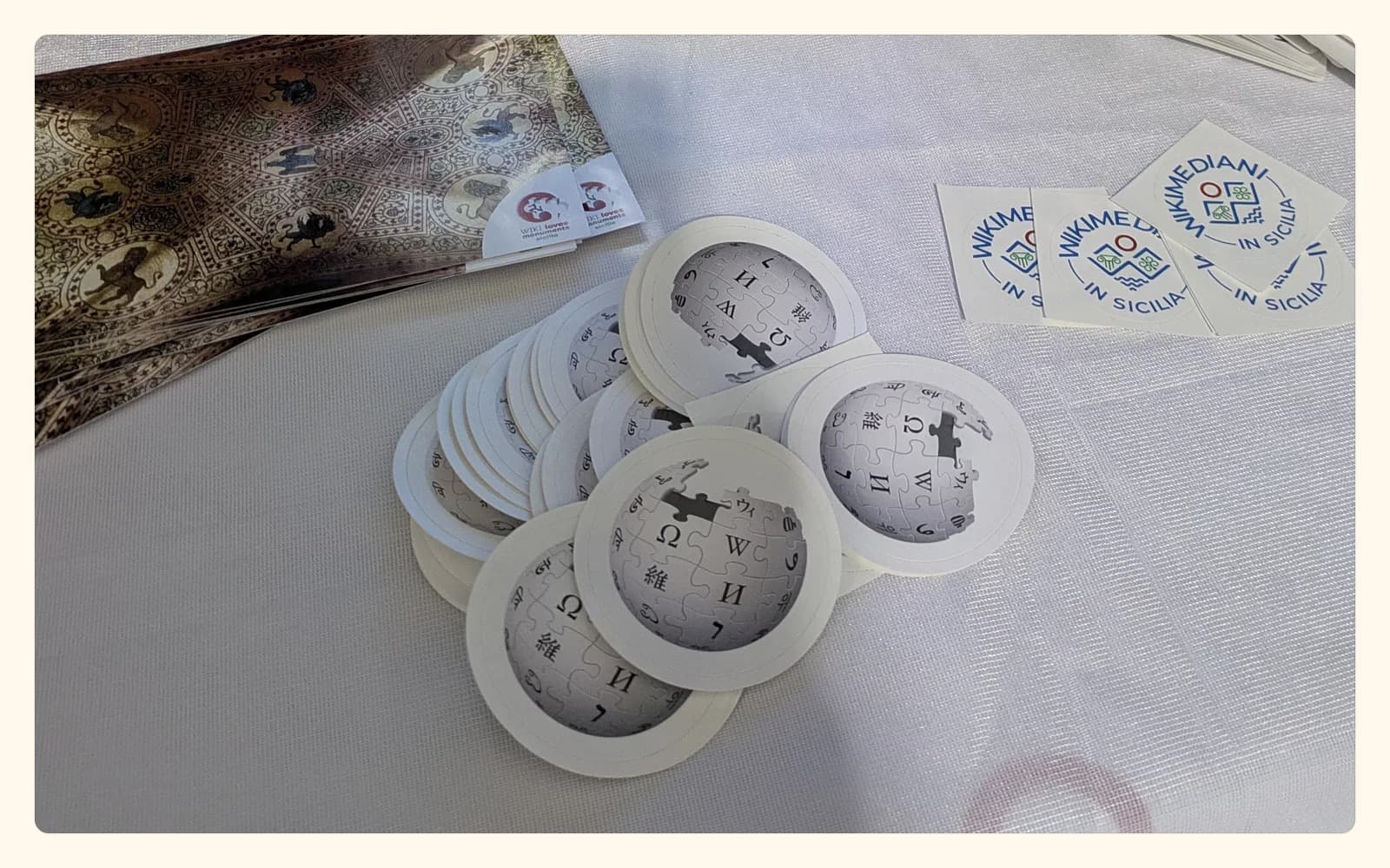 A Catania workshop table with Wikimedia badges, printed local cards, and editing materials; no attendees are visible.