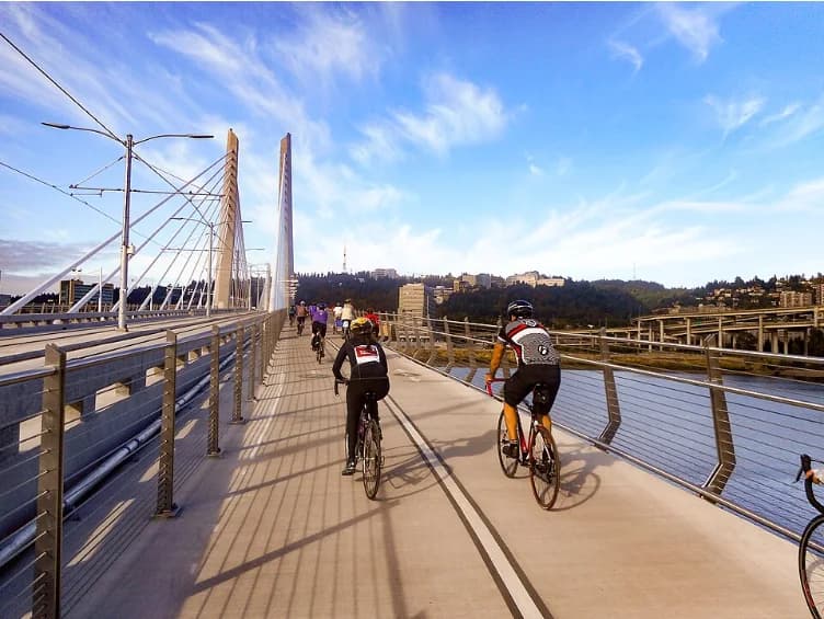Cyclists ride along Portland's Tilikum Crossing in daylight, with the city beyond the bridge.