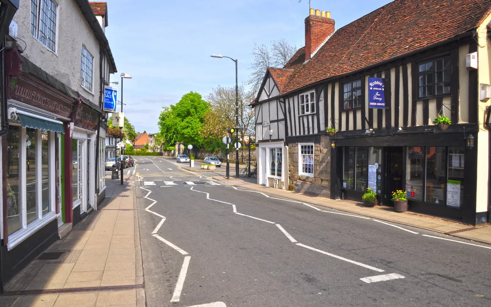 Independent storefronts and a black-and-white timbered building along Smith Street in Warwick on a clear day.