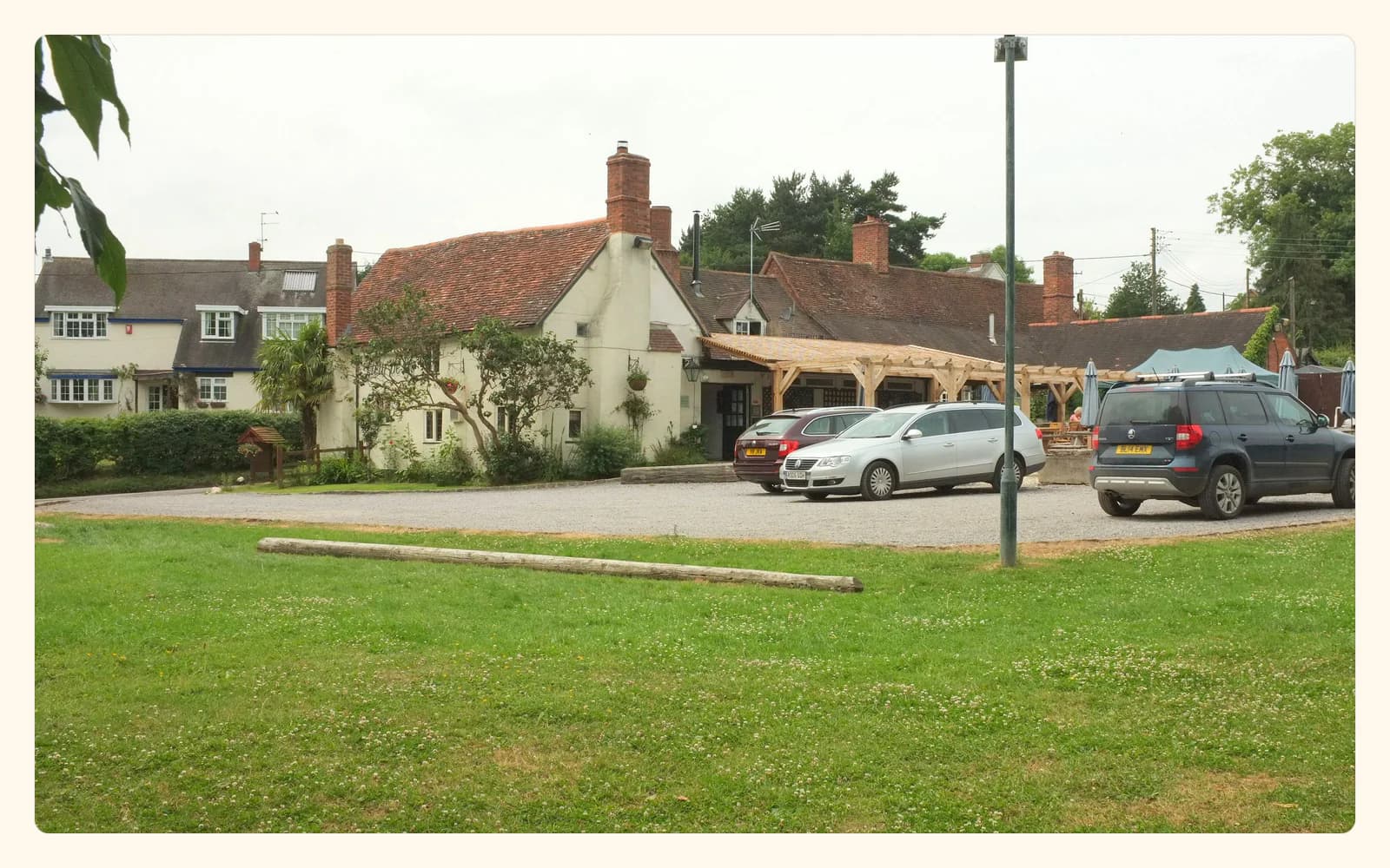 A low white pub with tiled roofs, brick chimneys, a covered terrace, and lawn in Lowsonford.
