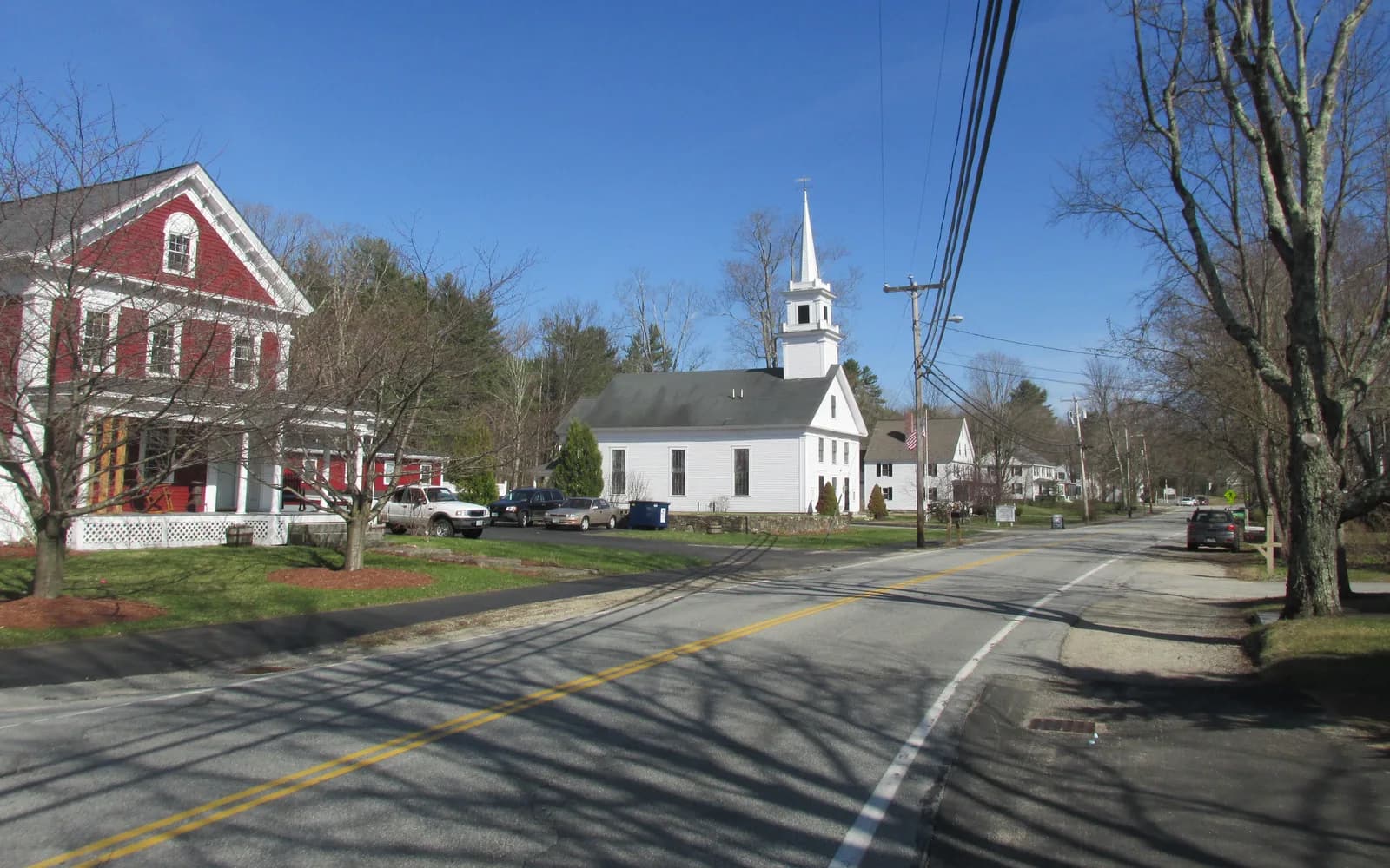 A white church, a red clapboard building, leafless trees, and a road on Main Street in Brookline, New Hampshire.